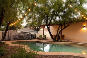 A swimming pool with a surrounding deck, a covered seating area, and string lights. - The Tucson Bungalow Designer Sam Hughes Retreat (Tucson)