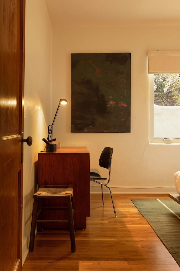 A room with a wooden desk, a chair, a lamp, and a large abstract painting on the wall. - The Tucson Bungalow Designer Sam Hughes Retreat (Tucson)