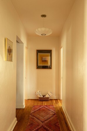 A hallway with a patterned rug, a framed artwork, and a basket with folded items. - The Tucson Bungalow Designer Sam Hughes Retreat (Tucson)