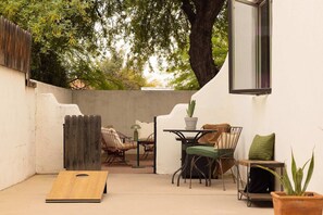 A patio area with a table and chairs, a wooden board, and a potted plant. - The Tucson Bungalow Designer Sam Hughes Retreat (Tucson)