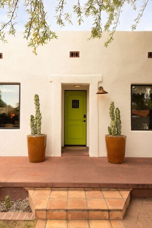 Un bâtiment avec une porte verte, deux grands cactus en pot et une fenêtre sur le côté gauche.