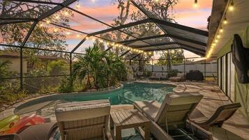 A covered outdoor area with a pool, lounge chairs, and string lights.