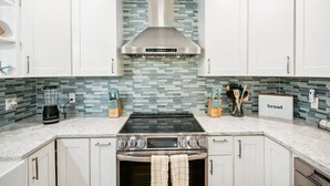 Una cocina moderna con armarios blancos, una campana extractora de acero inoxidable, horno empotrado y salpicadero de azulejos.