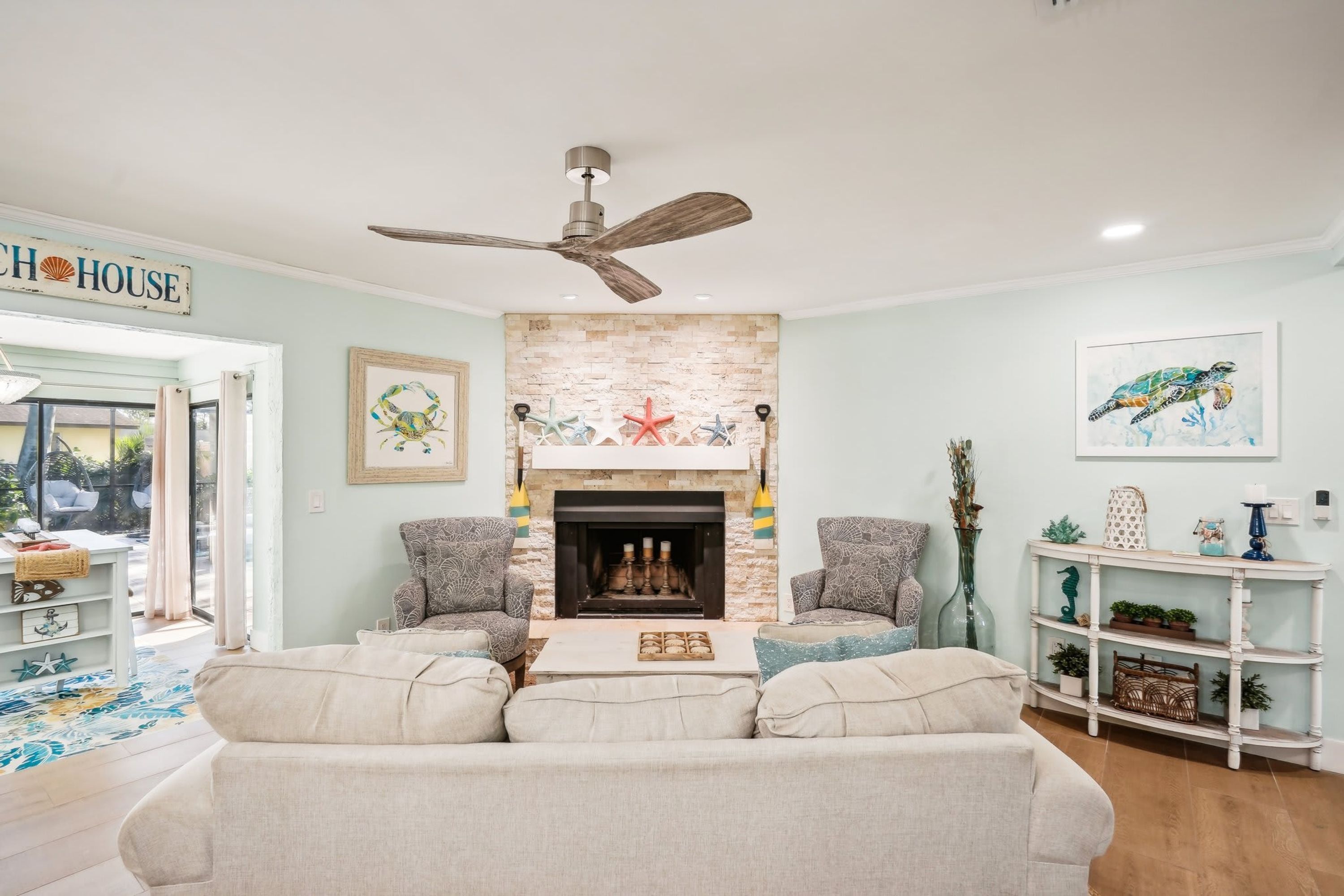 Un salon avec une cheminée, deux fauteuils, un canapé et un ventilateur de plafond.