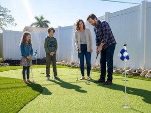 A family playing golf on a well-maintained lawn with a white fence in the background. - 4 Br Bradenton Home Private Pool Outdoor Bar W D (Bradenton)