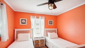 Una habitación con dos camas individuales, un ventilador de techo y dos cuadros colgados.