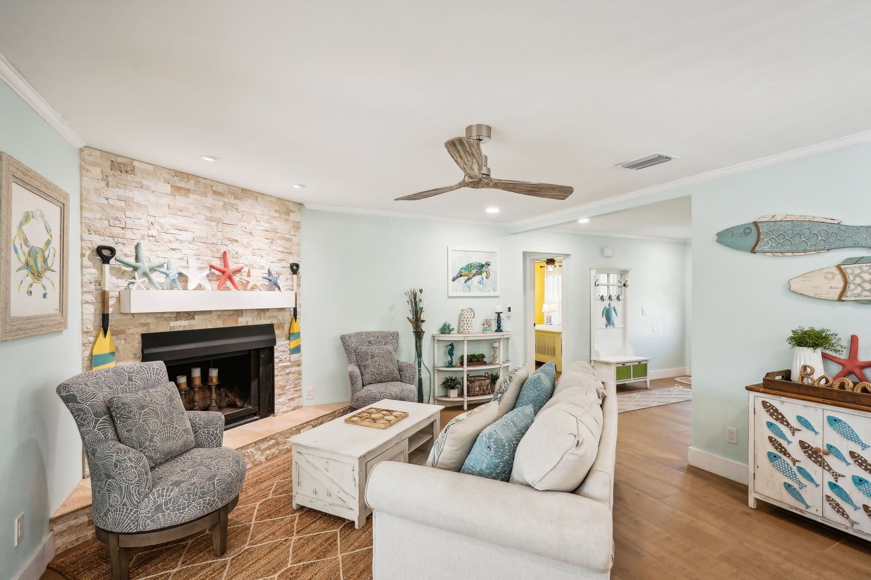 A living room with a fireplace, a ceiling fan, and nautical-themed decor.
