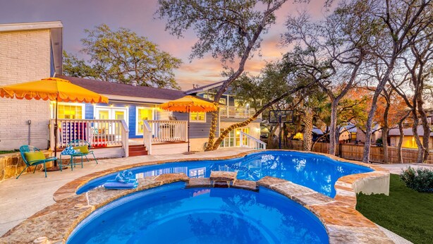 A backyard with a swimming pool, a covered patio, and a house with a brick exterior. - The Sunburst Sleeps 18 Basketball Heated Pool (San Antonio)