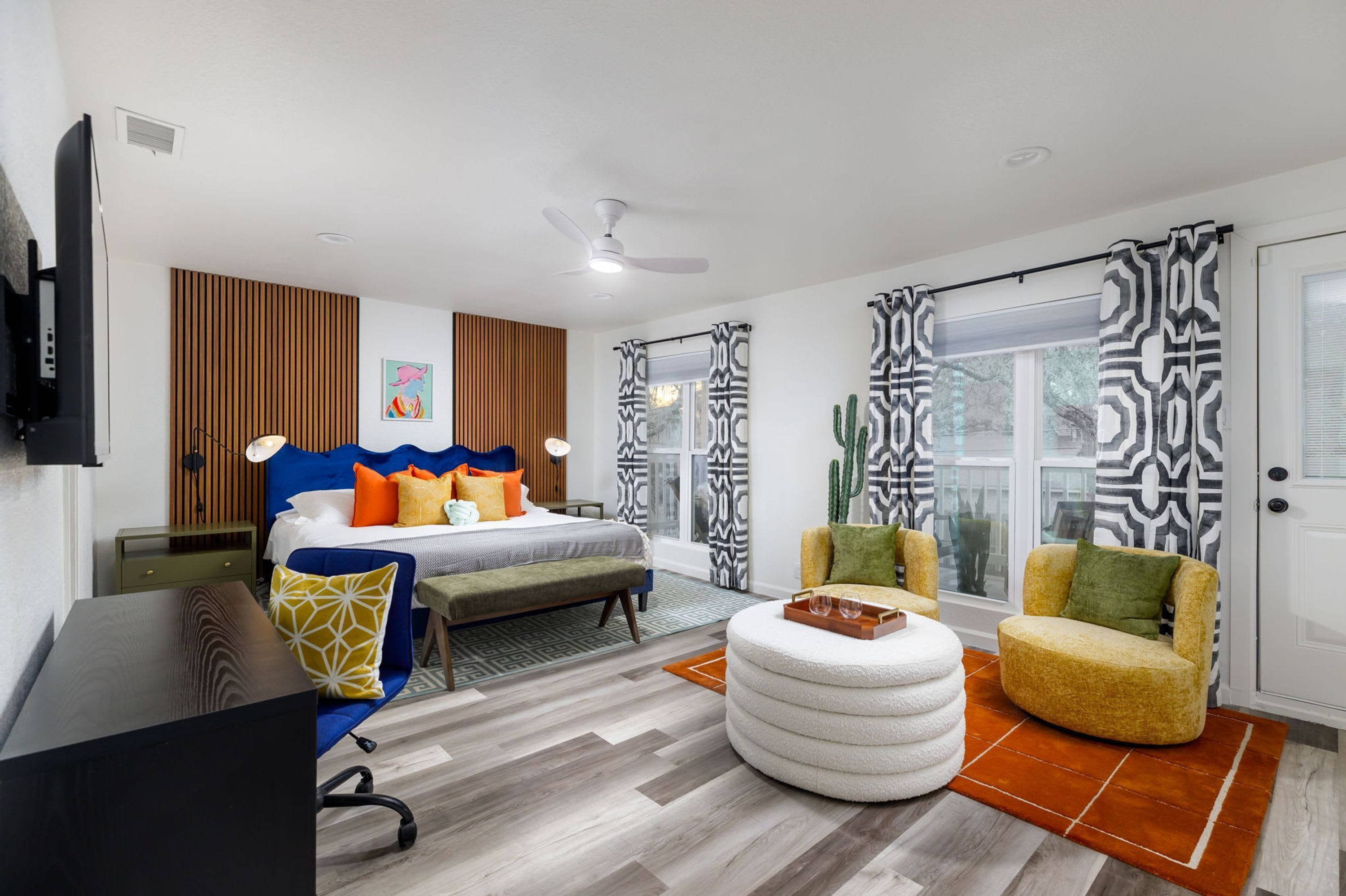 Un dormitorio moderno con cama, escritorio, silla, banqueta redonda y ventana con cortinas estampadas.