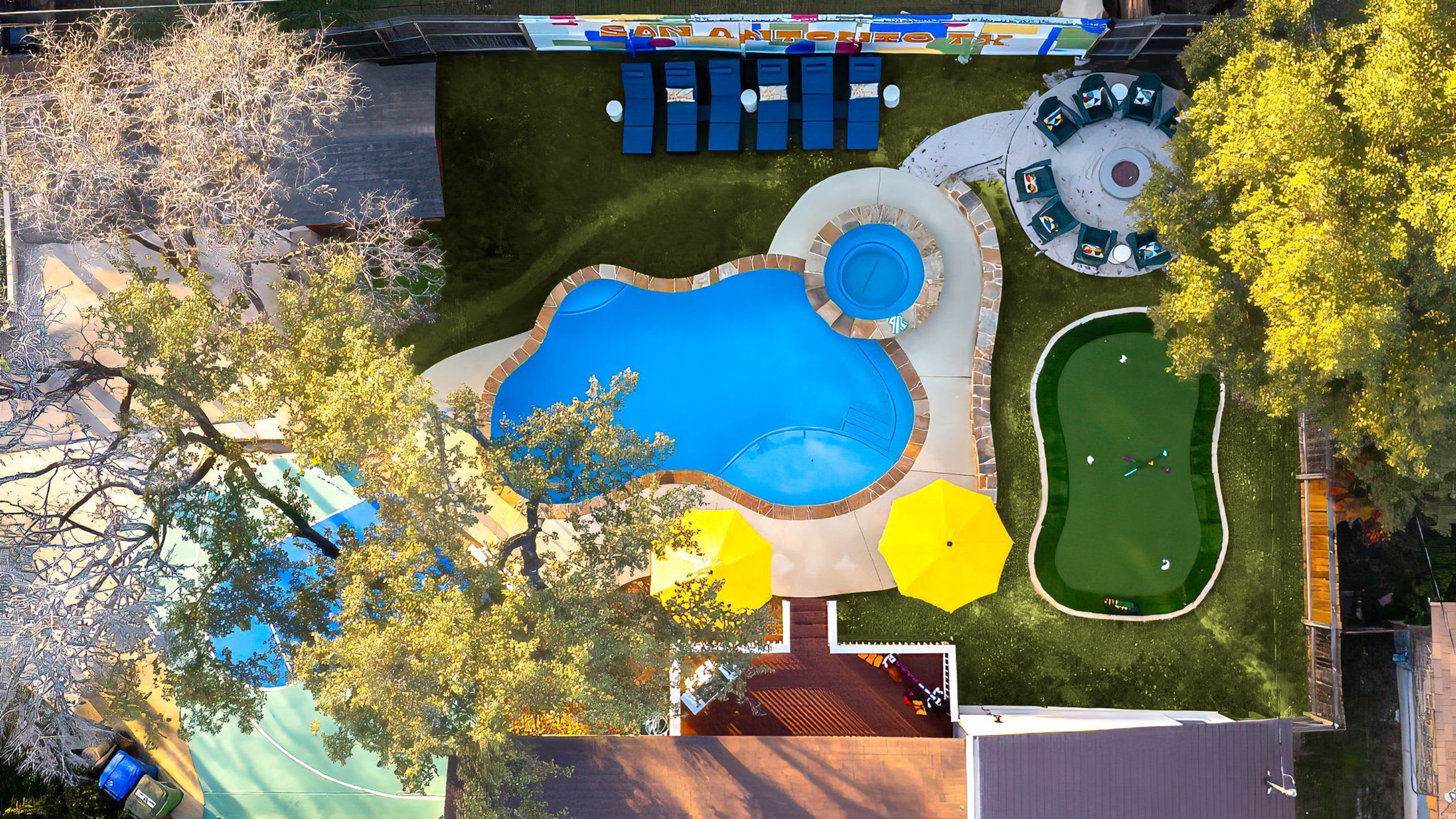 Un área de piscina con una piscina grande, una piscina rectangular más pequeña y un campo de práctica de golf.