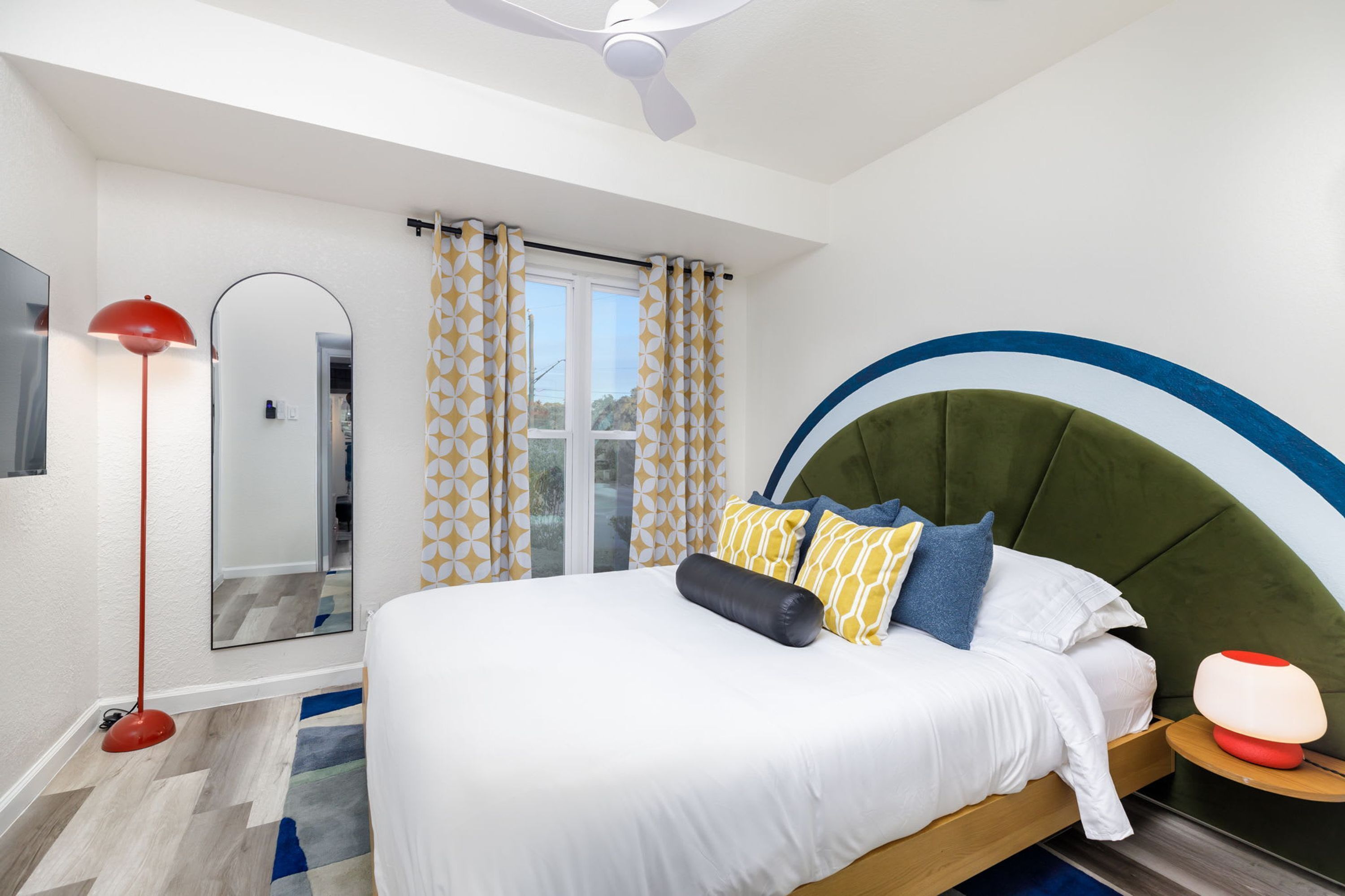 Ein Schlafzimmer mit Bett, Nachttischlampe, Spiegel und Deckenventilator.