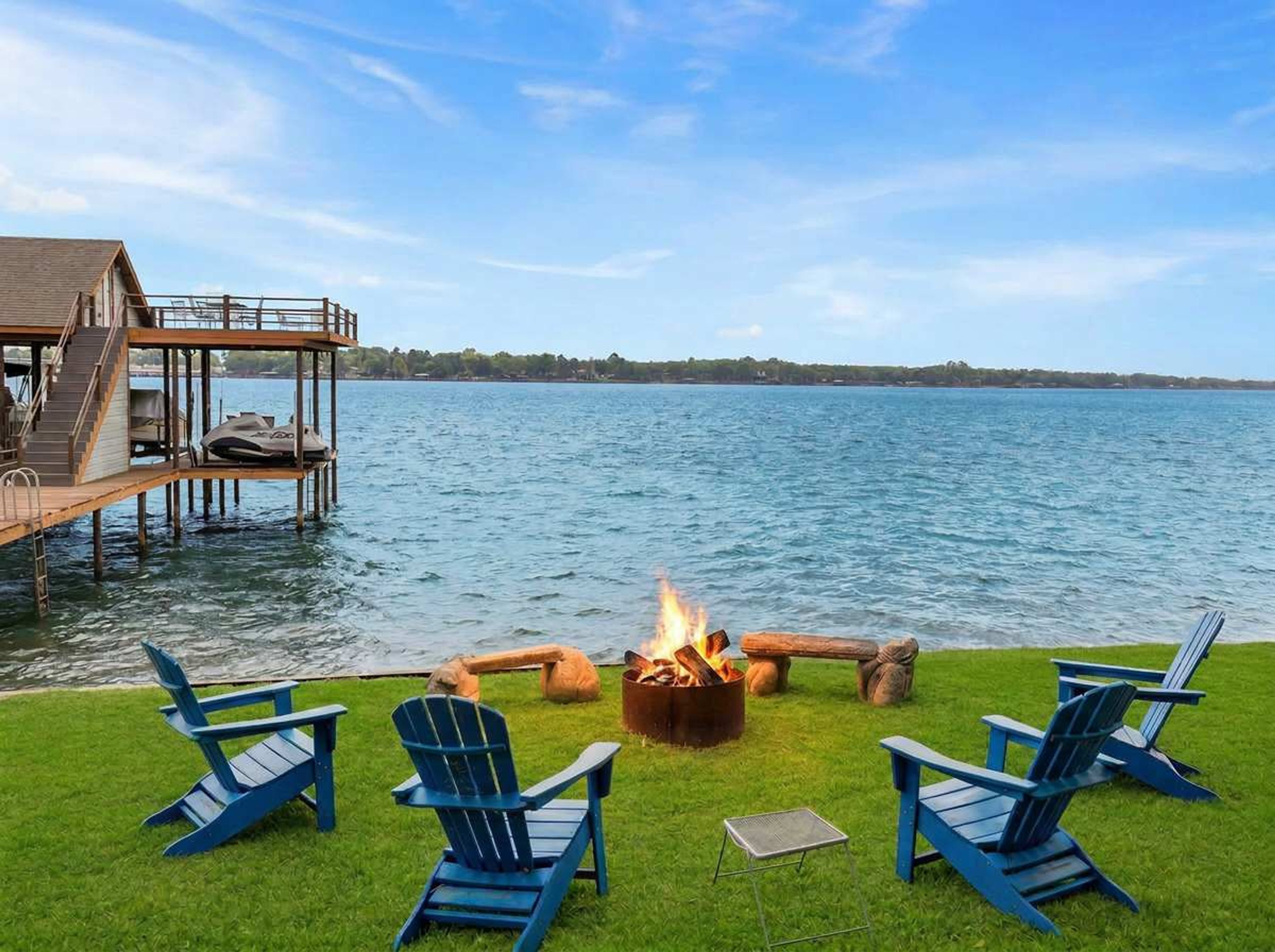 Een terras aan het meer, met een vuurkuil en Adirondack-stoelen.