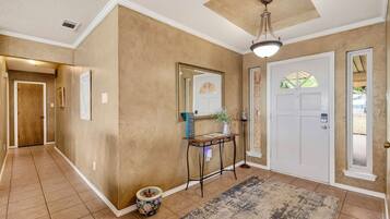 A hallway with a door, a mirror, a small table with a vase, and a rug.