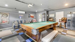 Una sala con piscina, mesa de billar, sofá, silla y refrigerador.