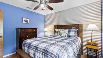 A bedroom with a bed, a nightstand, a lamp, a ceiling fan, and a picture on the wall.