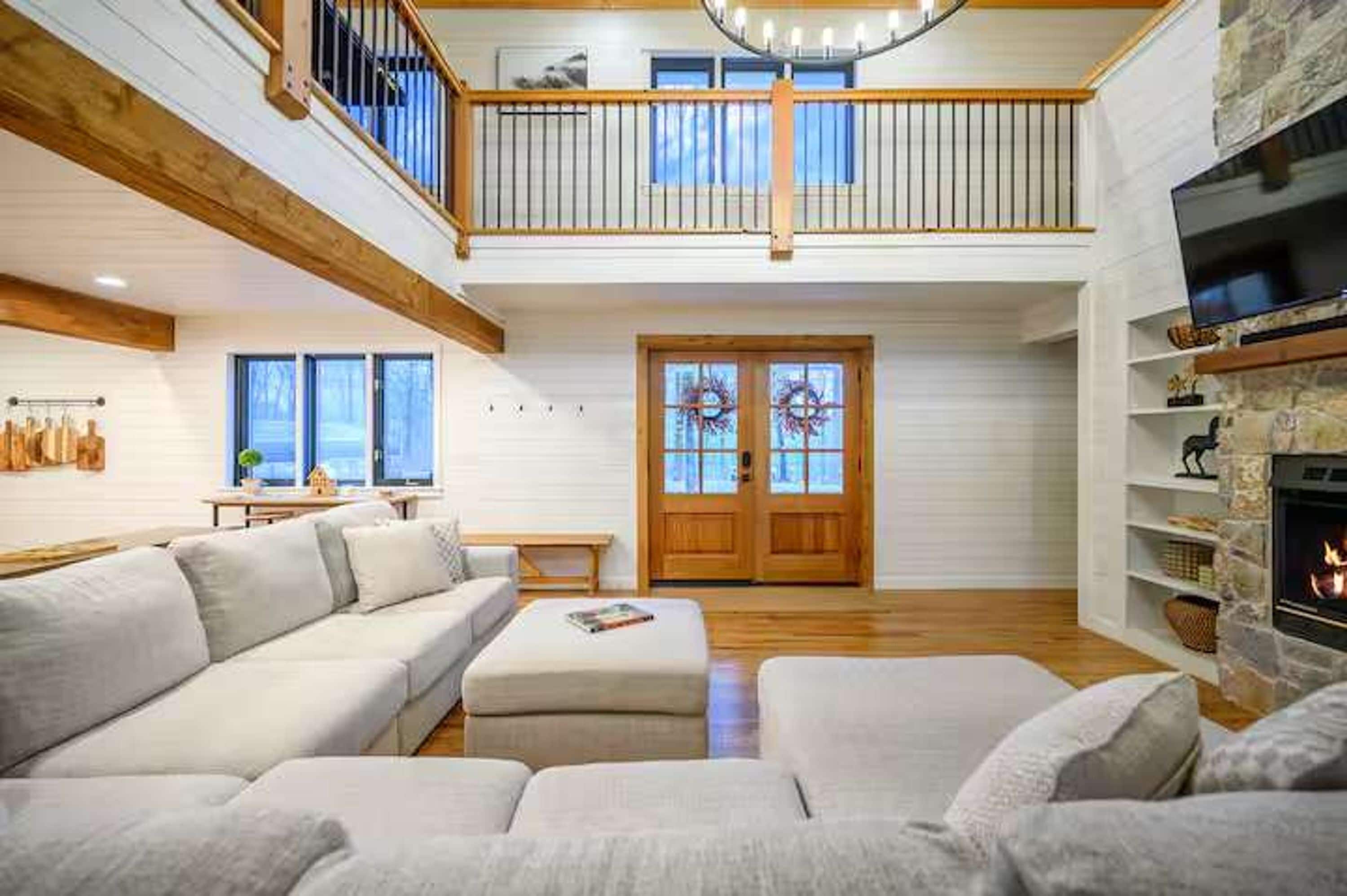 A spacious living room with a high ceiling, a fireplace, and a balcony.