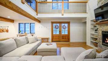 A spacious living room with a high ceiling, a fireplace, and a balcony.