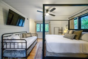Un dormitorio con una cama, una cama adicional, un ventilador de techo, una ventana y un televisor montado en la pared.