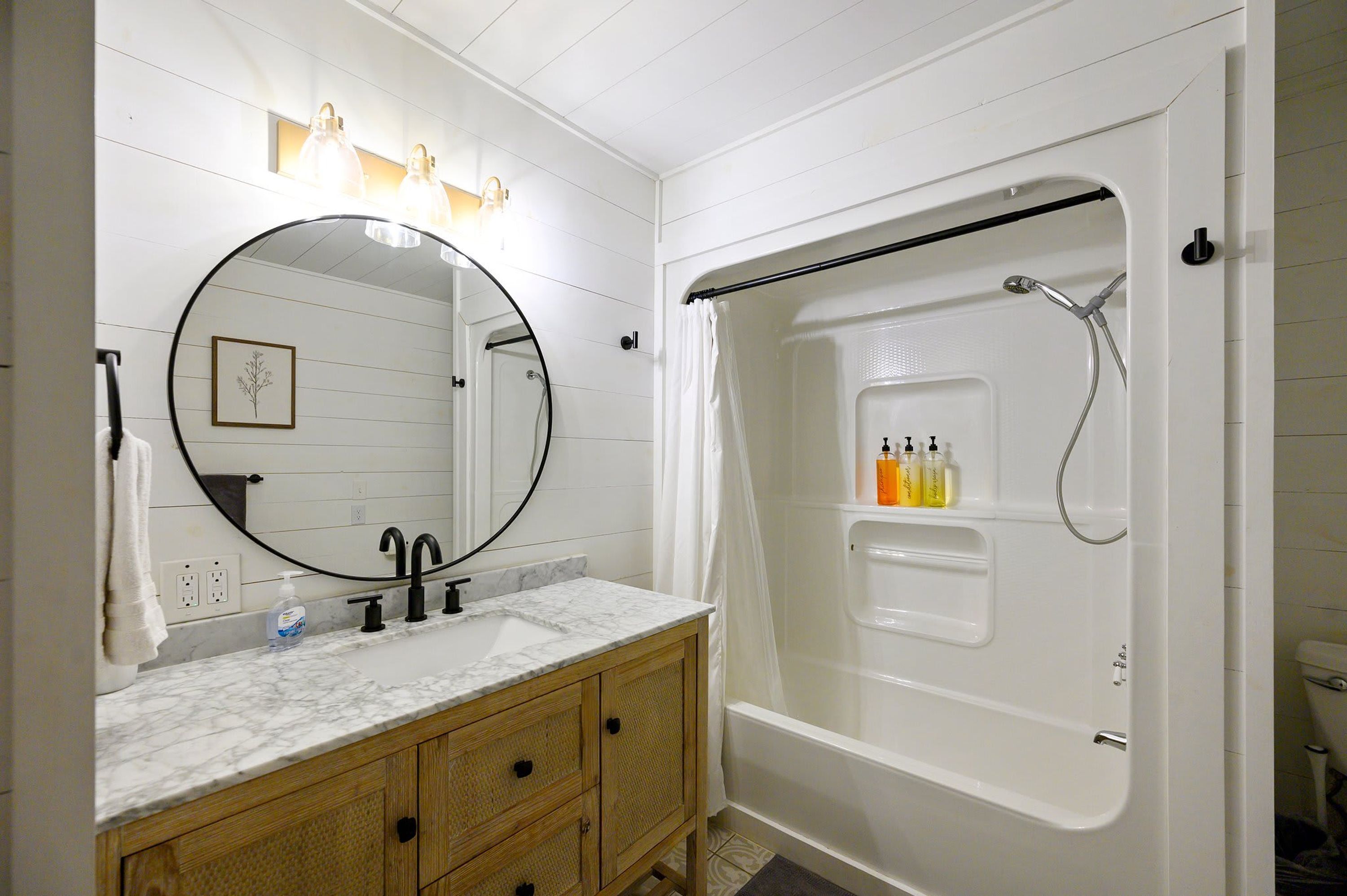 Een badkamer met een wit wastafelmeubilair, een grote spiegel, een douche met glazen deur en een handdoekrek.