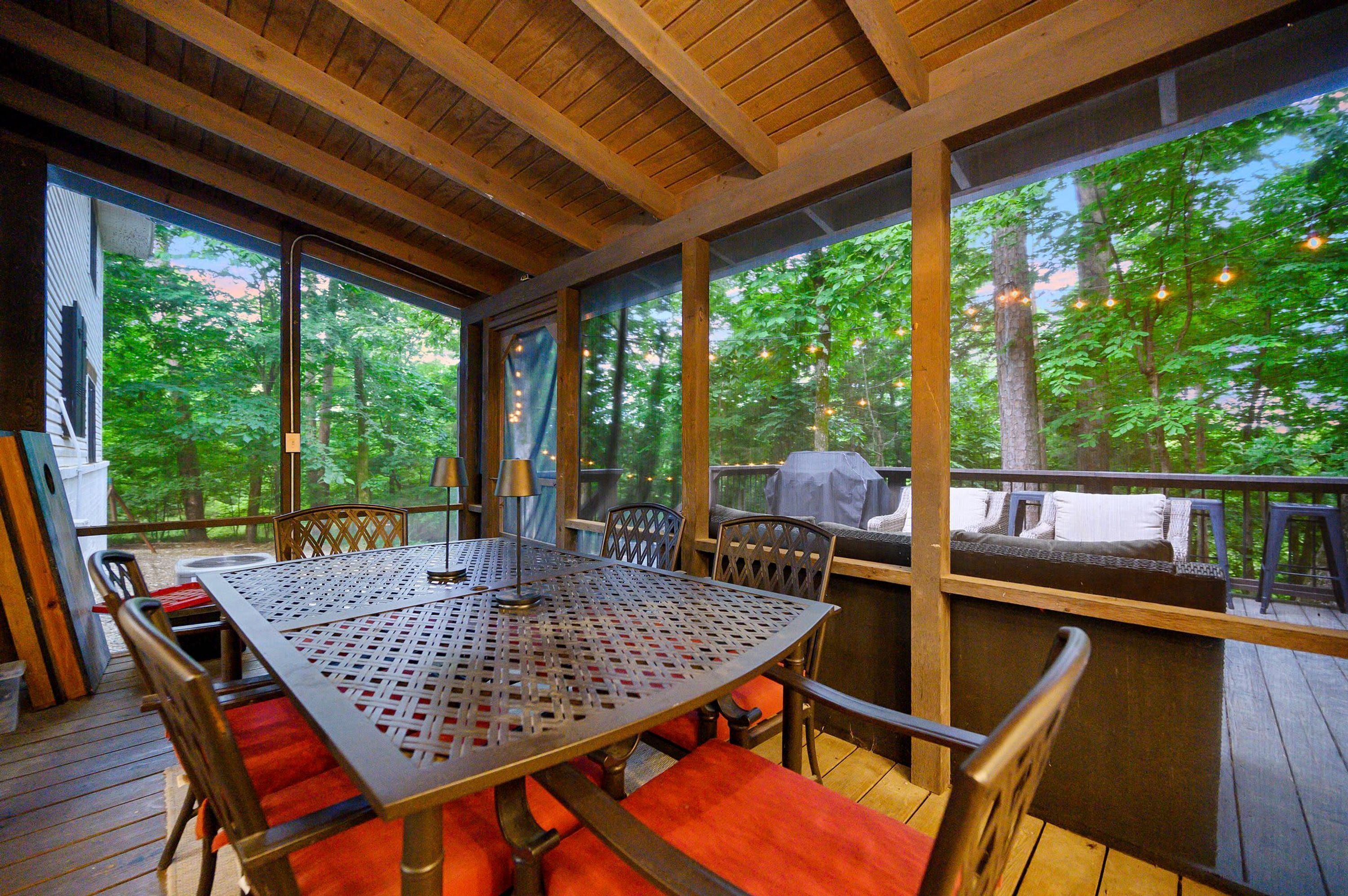 Un área de comedor al aire libre con una mesa y sillas, ventanas amplias y vistas a árboles.