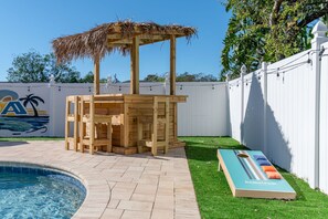A wooden structure with a thatched roof, a pool, and a lounge chair with a branded mattress. - Paradise Htd Pool Tiki Bar Hot Tub Games (Seminole)
