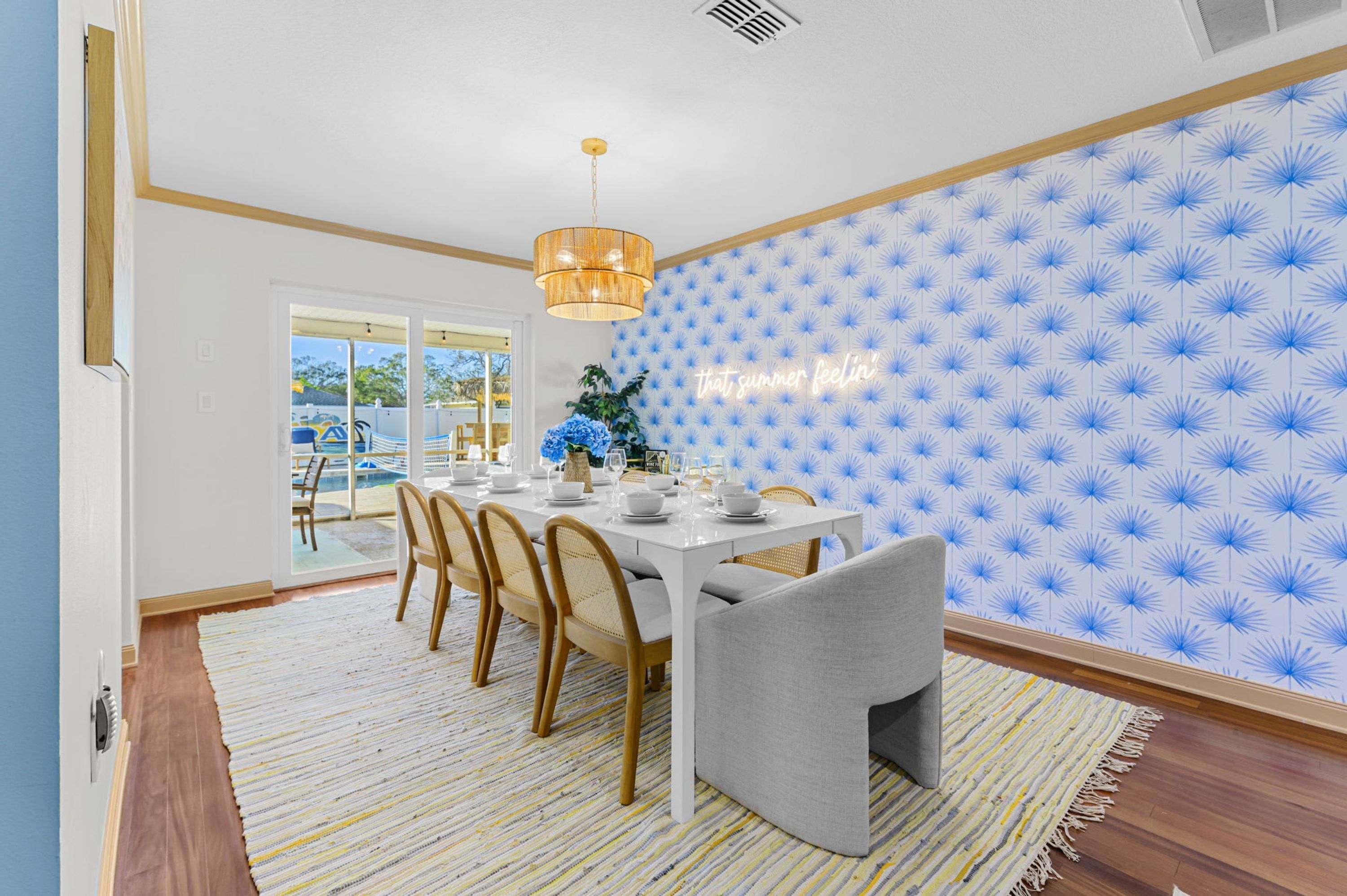 Un coin repas avec une table dressée pour quatre personnes, un lustre et un mur orné d’un motif.