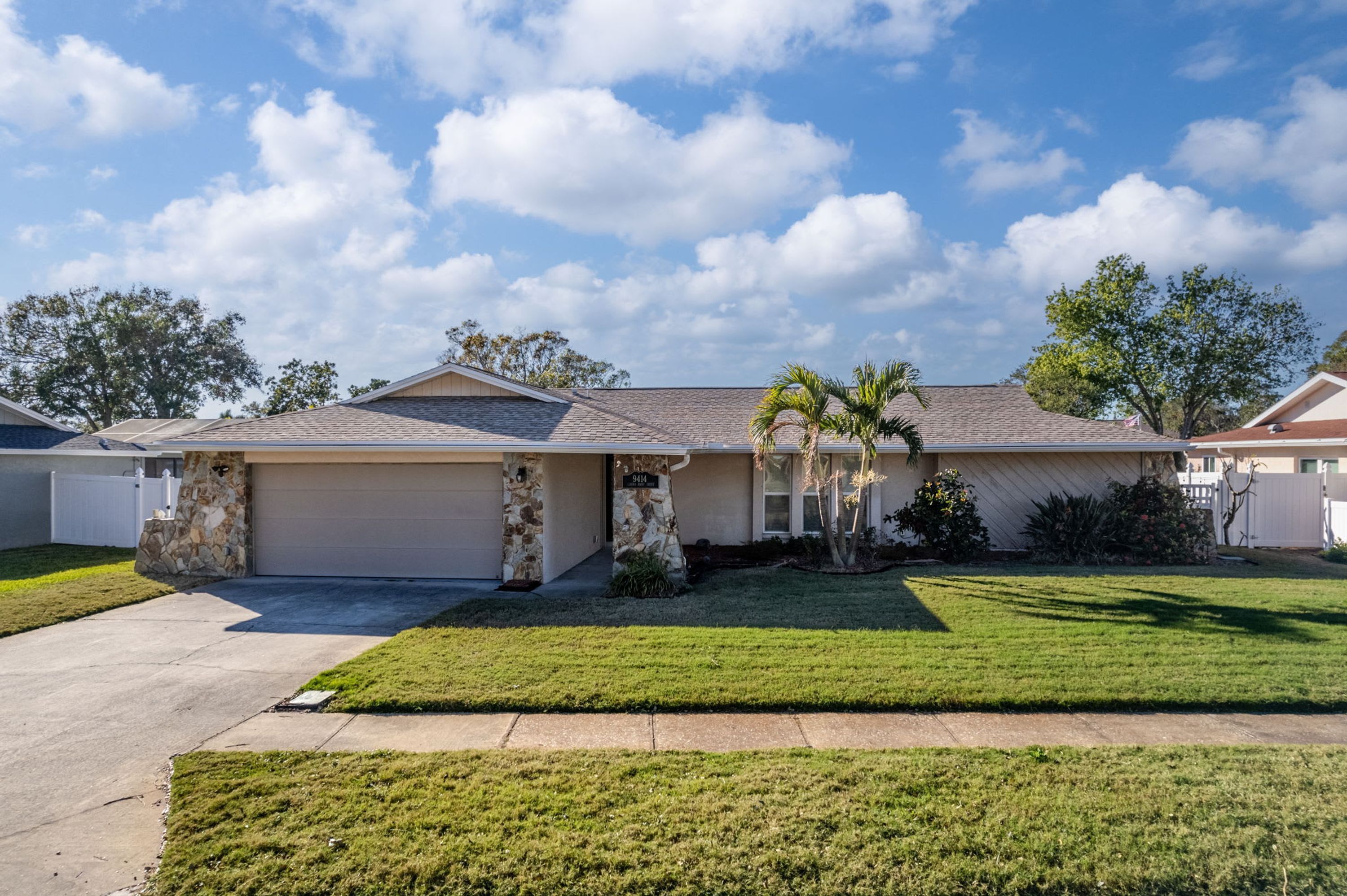 A single-story house with a garage, stone foundation, and a well-maintained lawn.