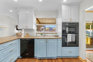 A kitchen with light blue cabinets, a dishwasher, a refrigerator, and a window overlooking a patio area. - Paradise Htd Pool Tiki Bar Hot Tub Games (Seminole)