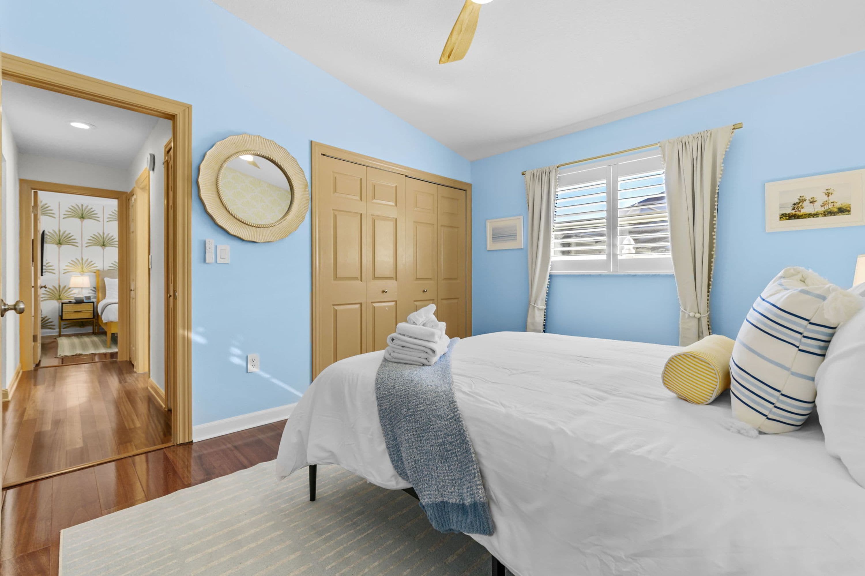 Een slaapkamer met een bed, een deur, een raam met gordijnen en een spiegel aan de muur.