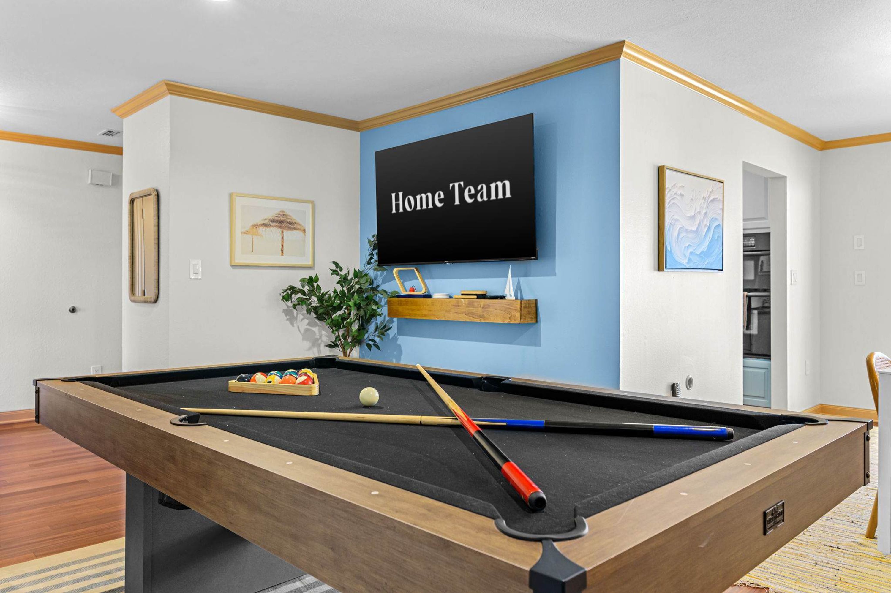 A pool table with balls and cues, a mounted television displaying 'Home Team', and a framed picture on the wall.