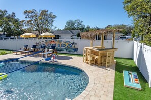 A swimming pool with lounge chairs and a wooden table, surrounded by a white fence and a mural. - Paradise Htd Pool Tiki Bar Hot Tub Games (Seminole)