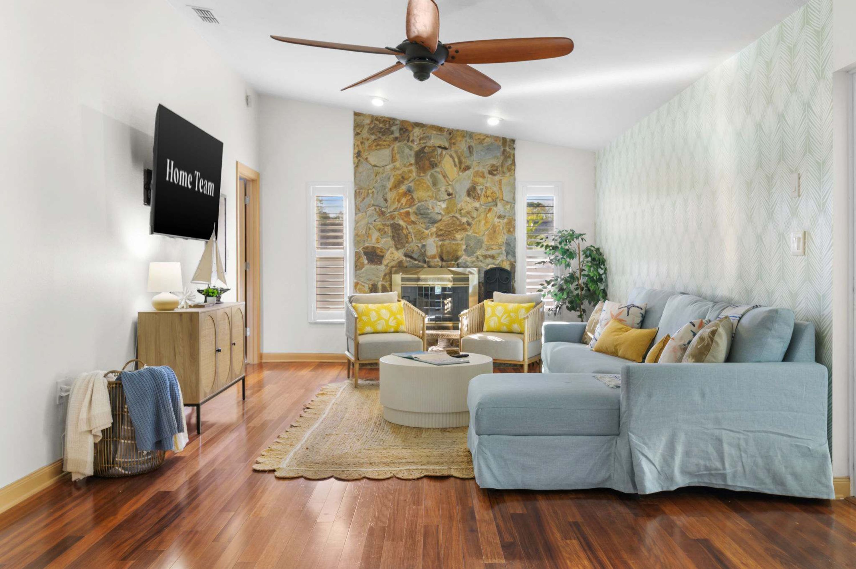 Un salon avec un ventilateur de plafond, un mur en pierre, un canapé, une table basse et un téléviseur.
