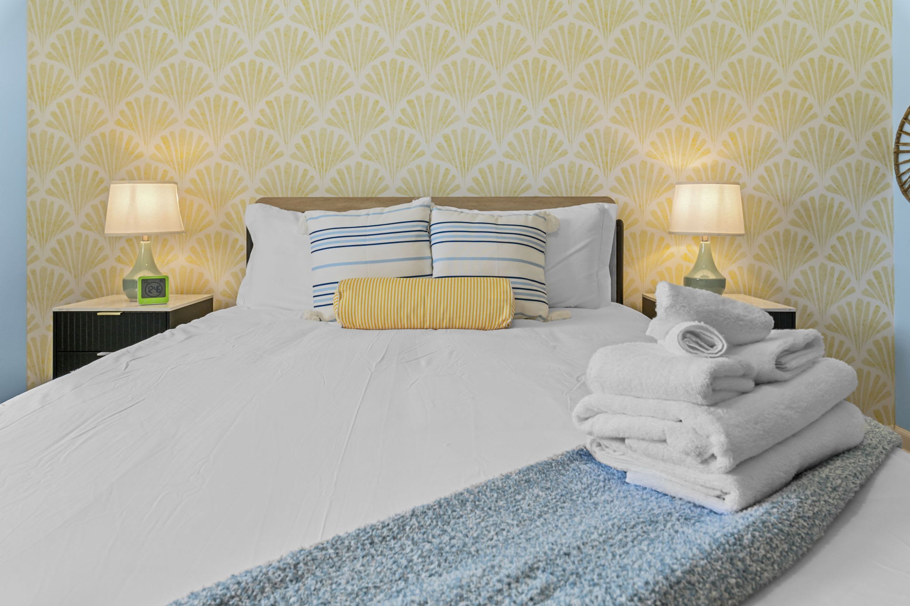 A neatly made bed with pillows, a folded towel, and a bedside lamp on a nightstand.
