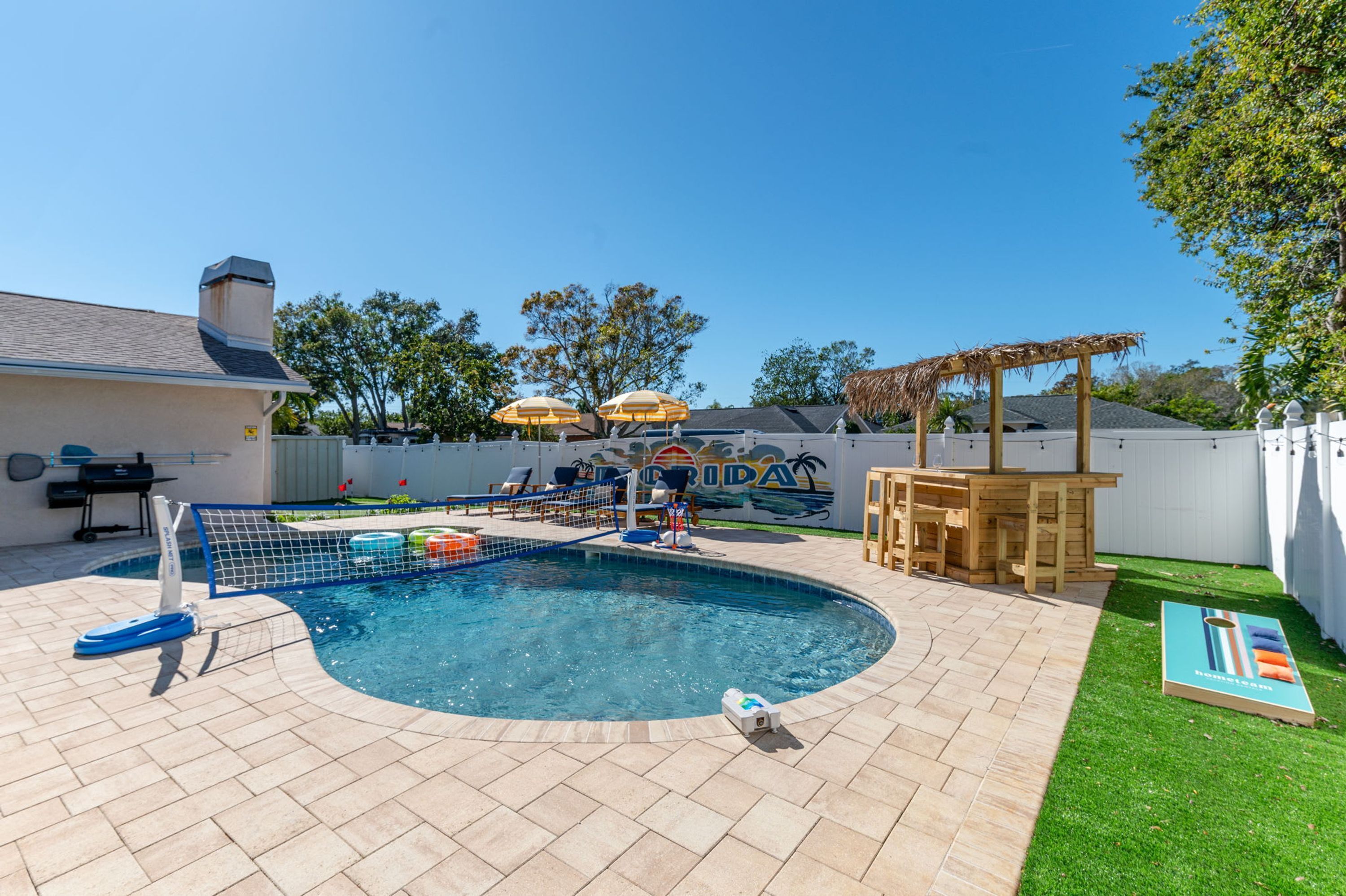 A backyard with a swimming pool, lounge chairs, a barbecue grill, and a wooden pergola.