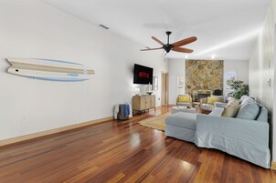 Una sala de estar moderna con piso de madera, ventilador de techo, televisor montado y pared de piedra.