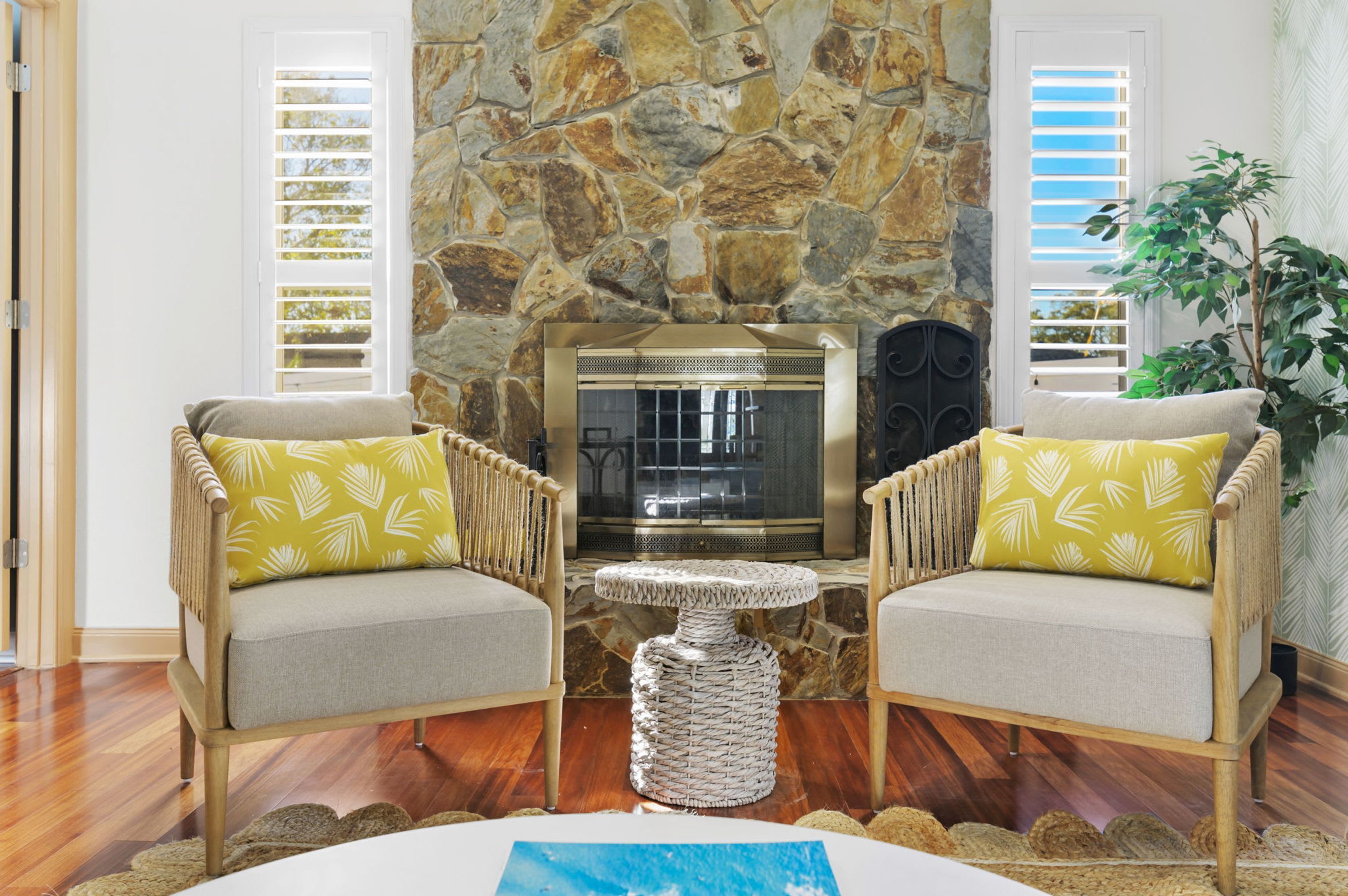 A room with a stone wall, two chairs with patterned cushions, a small round table, and a fireplace.