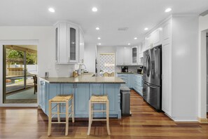 A modern kitchen with white cabinets, a stainless steel refrigerator, and a large island with stools. - Paradise Htd Pool Tiki Bar Hot Tub Games (Seminole)