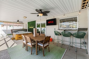 A covered outdoor area with a wooden table and chairs, a hot tub, and a wall-mounted TV screen displaying 'NETFLIX'. - Paradise Htd Pool Tiki Bar Hot Tub Games (Seminole)