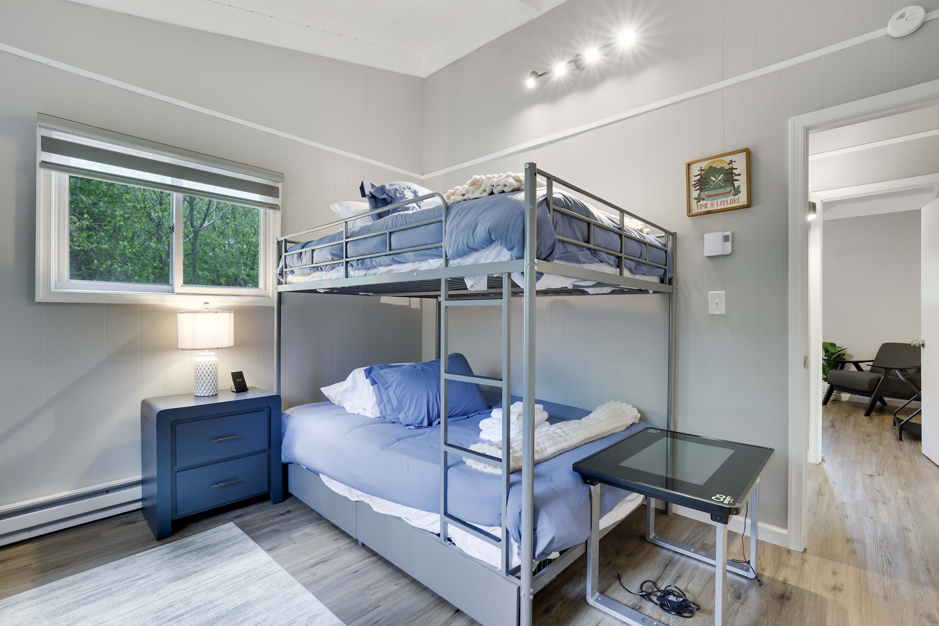 Habitación con literas, escritorio, mesita de noche, ventana y puerta que da a otra habitación.