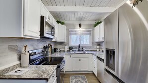 A modern kitchen with white cabinetry, stainless steel appliances, and a large window providing natural light. - Bluewood Escape Sauna Hot Tub Game Room (Tobyhanna)