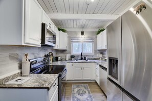 Una cocina moderna con armarios blancos, electrodomésticos de acero inoxidable y un amplio ventanal que proporciona luz natural.