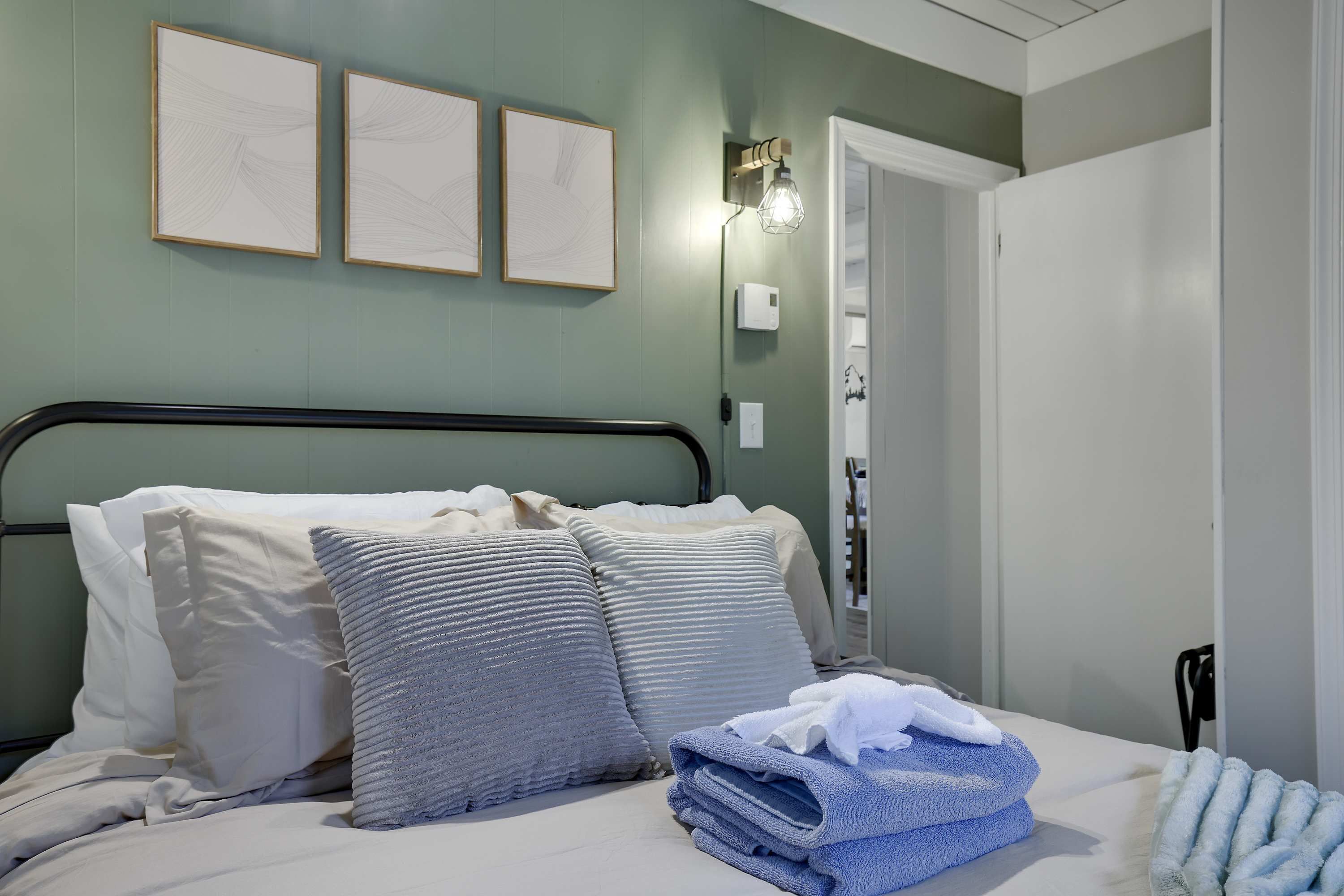 A neatly made bed with pillows and a stack of towels, a bedside lamp, and a door with a light switch.