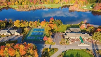 An aerial view of a residential area with a tennis court, a golf course, and a body of water.