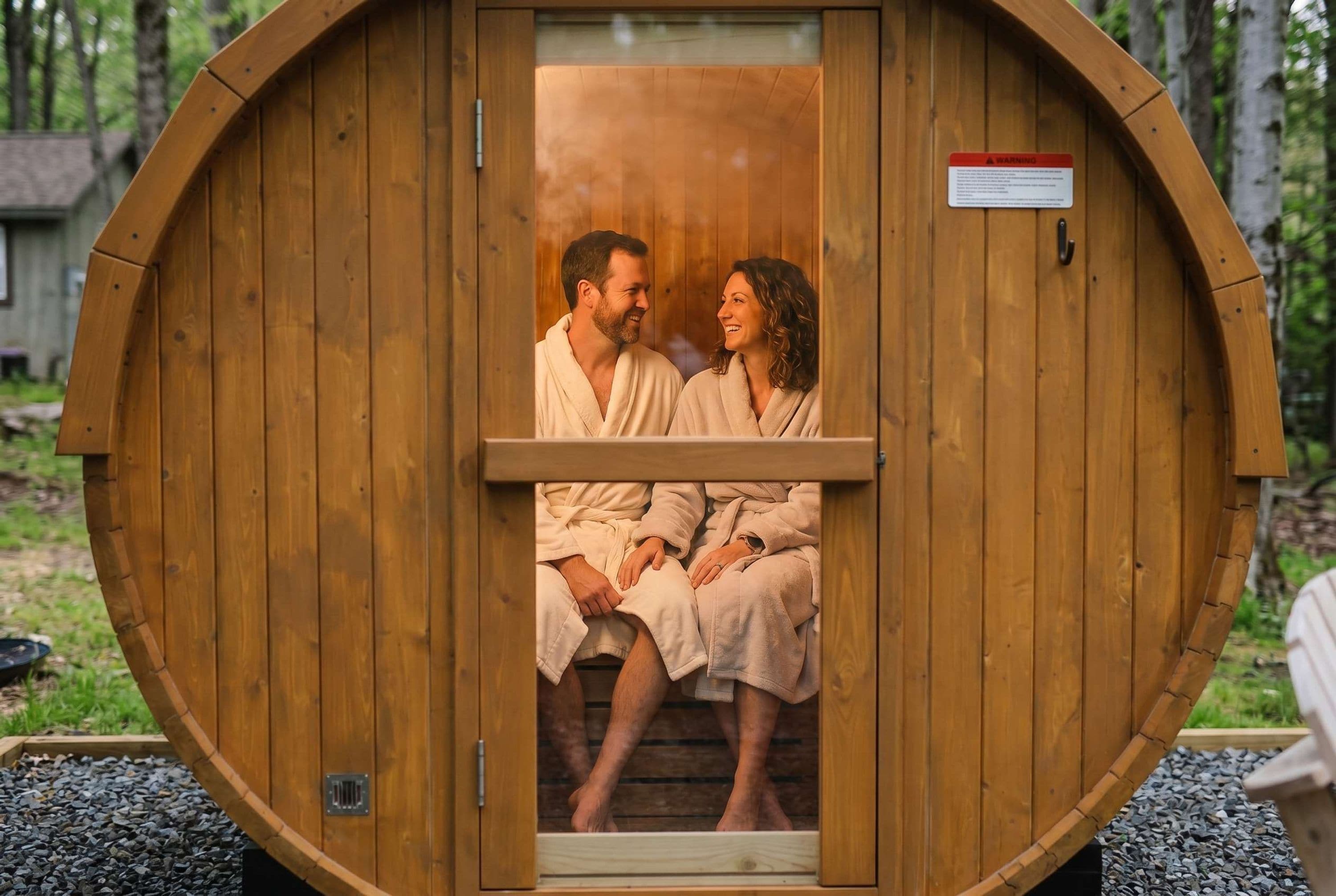 A wooden sauna with a door open, revealing two people sitting inside.