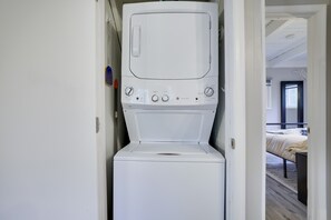 Una lavadora-secadora compacta instalada en un pasillo estrecho, con una cama visible en la habitación contigua.