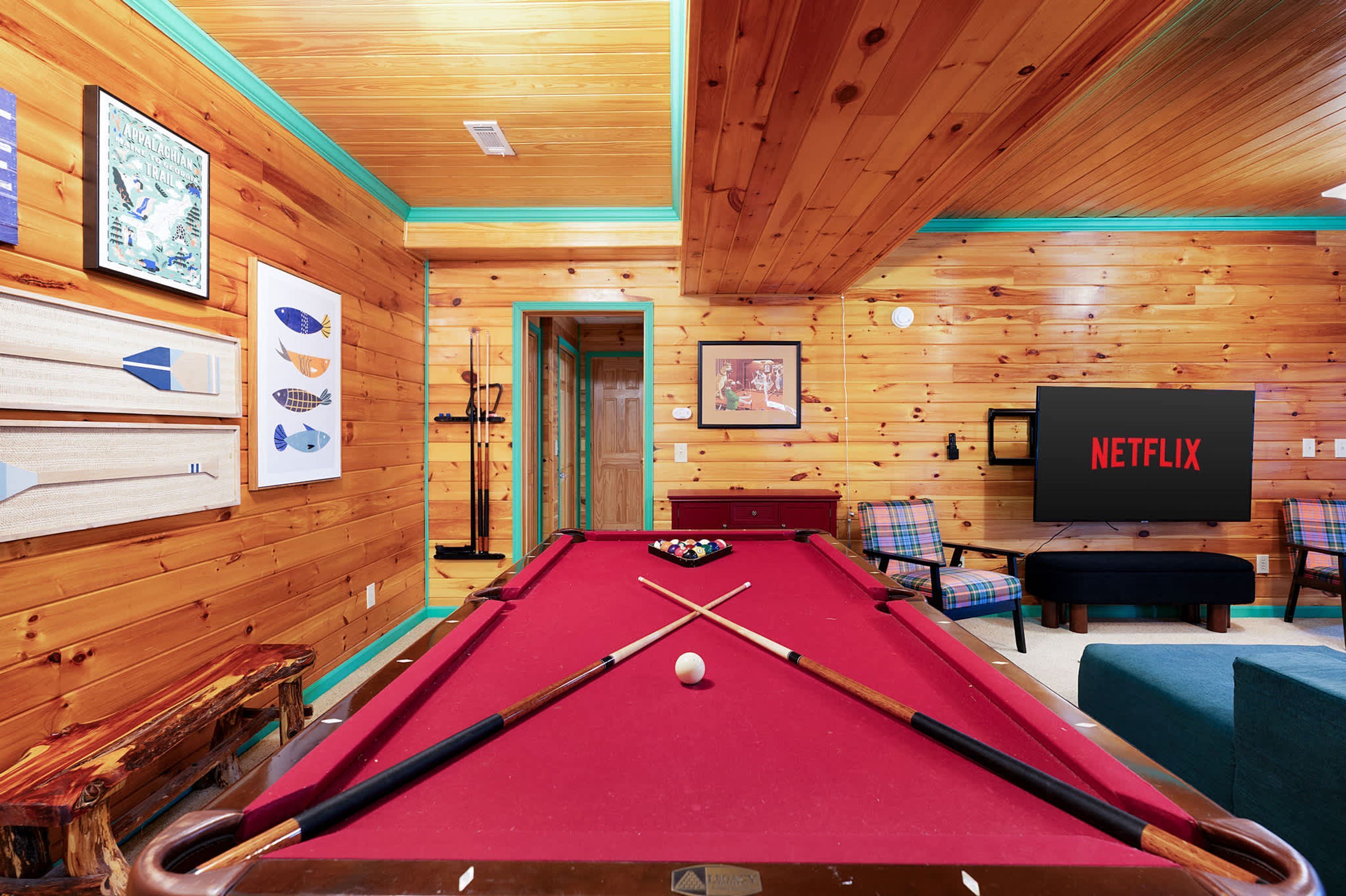 A pool table in a wooden room with a Netflix sign, framed artwork, and a door leading to another area.