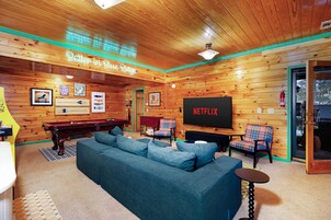 A cozy room with a wooden ceiling, a large flat-screen TV, a blue sofa, and a billiards table.