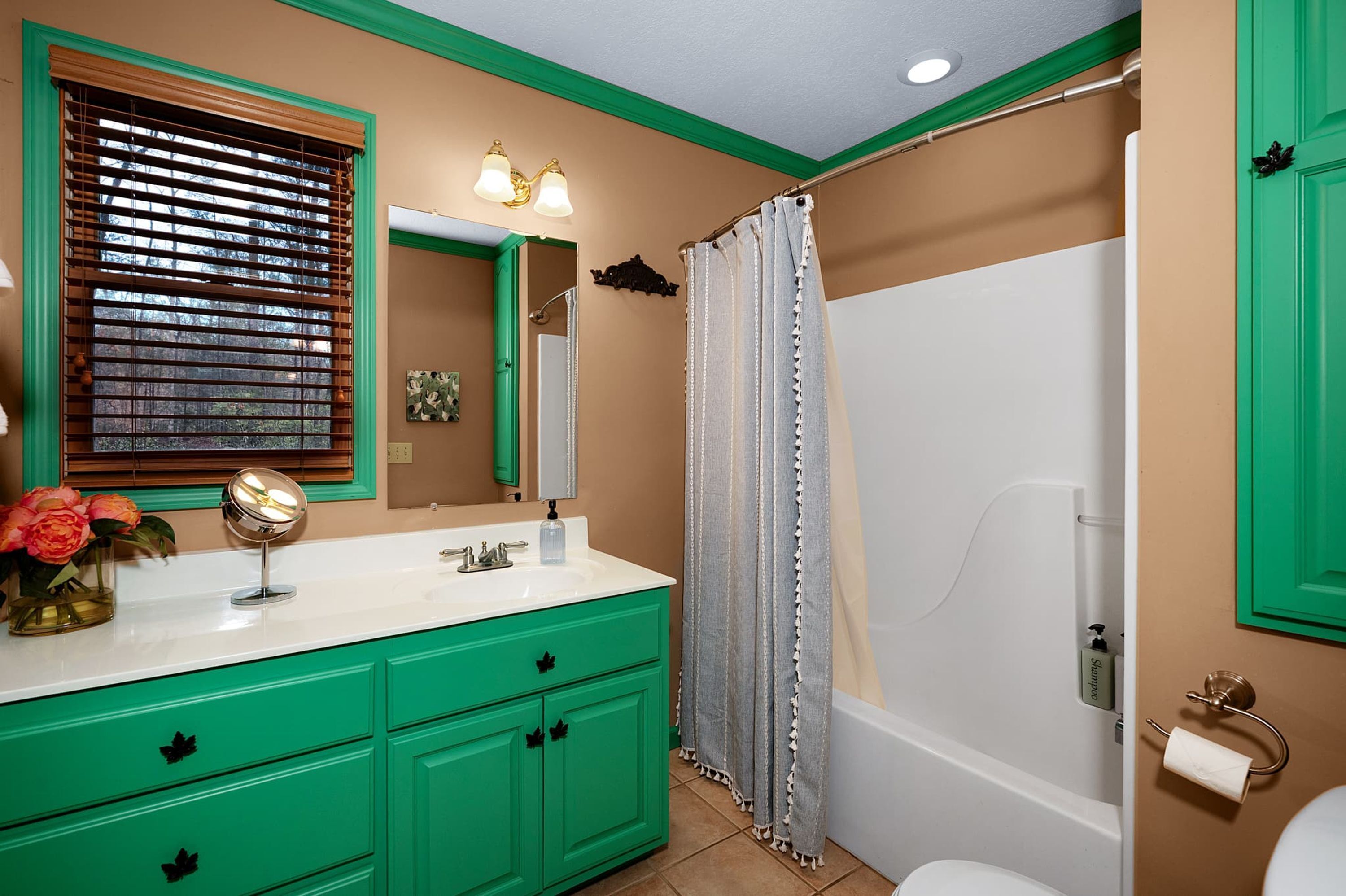 A bathroom with green cabinets, a white sink, a mirror, a shower curtain, and a toilet.