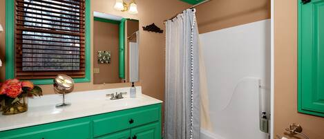 A bathroom with green cabinets, a white sink, a mirror, a shower curtain, and a toilet.