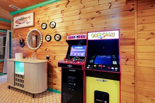 A wooden interior with arcade machines, a counter with glasses, and a wall with framed pictures.